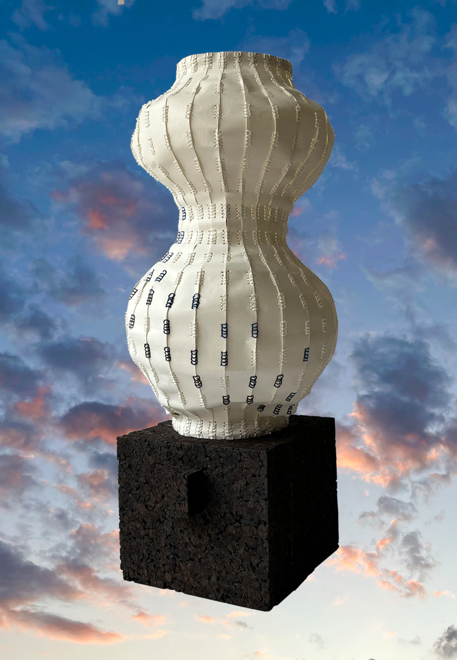 Decorative paper vessel with ribbed texture on a black cork base against a colorful sky